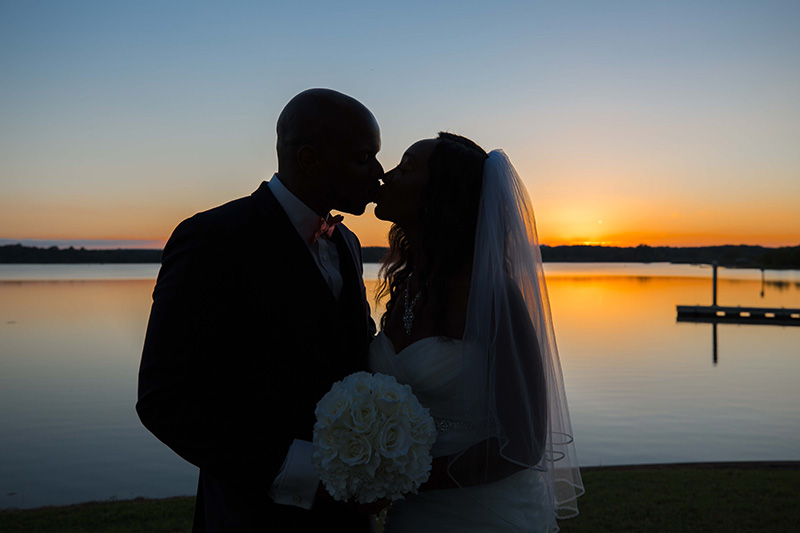 married couple kissing with bouquet at sunset