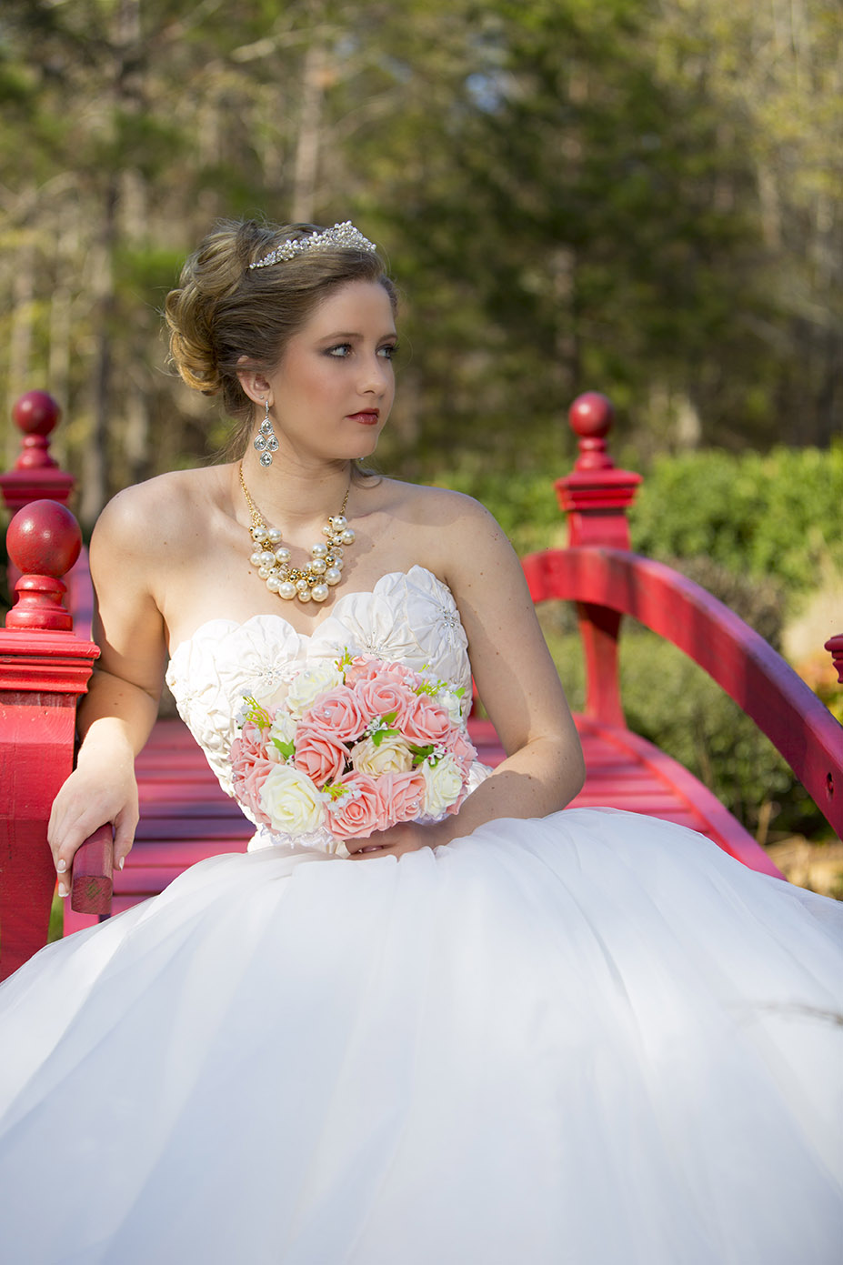 bride posing on a bridge with trees in background and flowers in hand