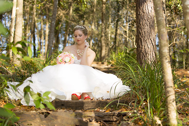 bride posing around trees in dress with flowers in hand