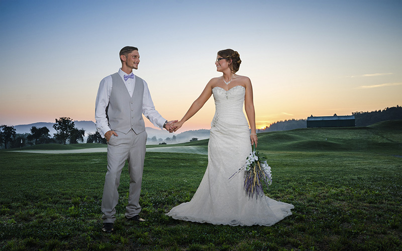 groom and bride posing outdoors in a field smiling and holding hands